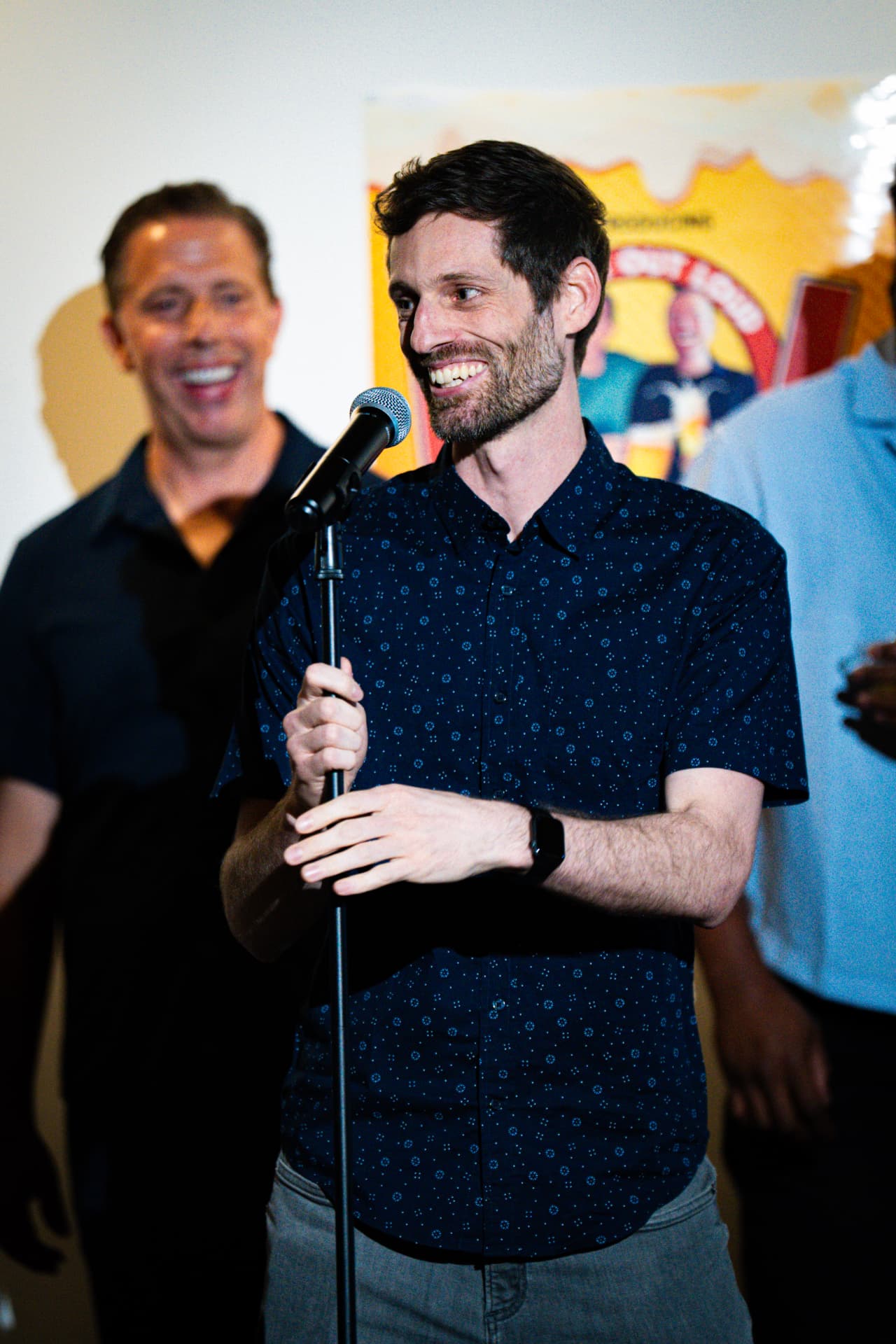 Comedian performing in front of the show poster